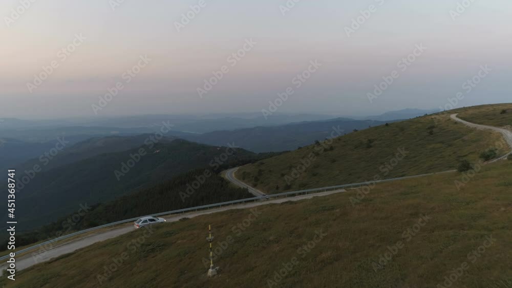 Drone follows car driving down a mountain pass road with deep valley background