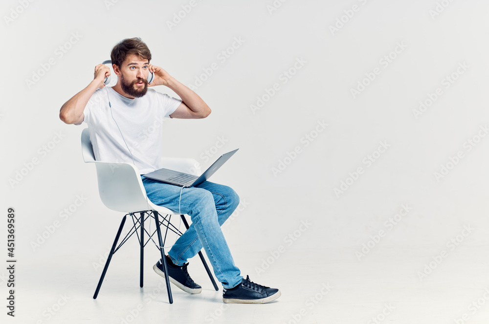 man in white t-shirt sitting on a chair with a laptop in headphones man in white t-shirt sitting on a chair with a laptop in headphones