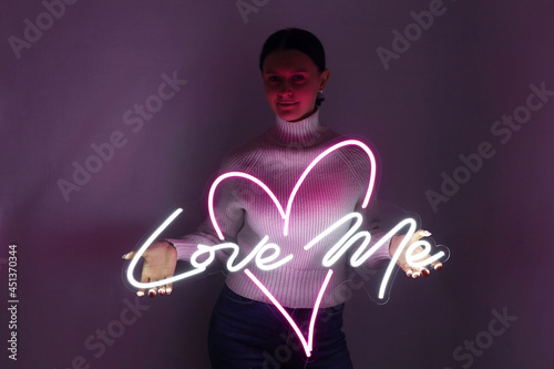 Beautiful girl with neon signs. White and pink neon heart with the inscription love me. Trendy style. Wedding design. Neon sign. Custom neon. Home decor.  photo