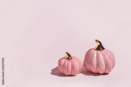 Two decorative ceramic pumpkins on pink background in hard light with copy space.