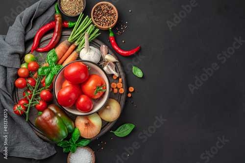 A set of vegetables and spices for cooking a vegetable dish, tomato sauce on a black background.