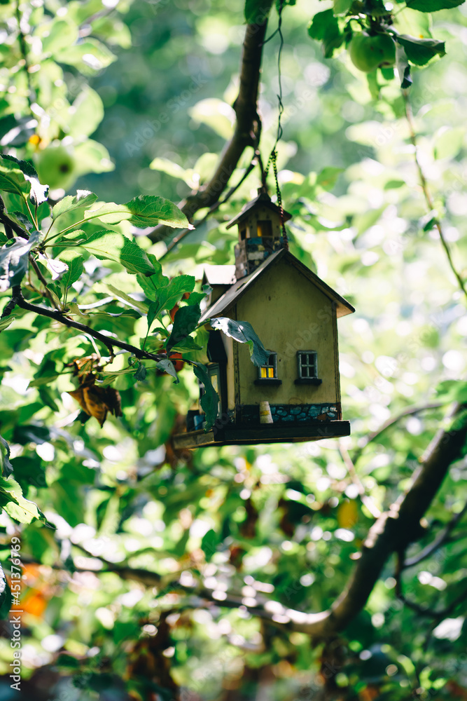 a feeder in the form of a house hanging from a tree