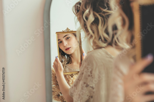 Young beautiful model girl with natural makeup looks at her reflection in the mirror