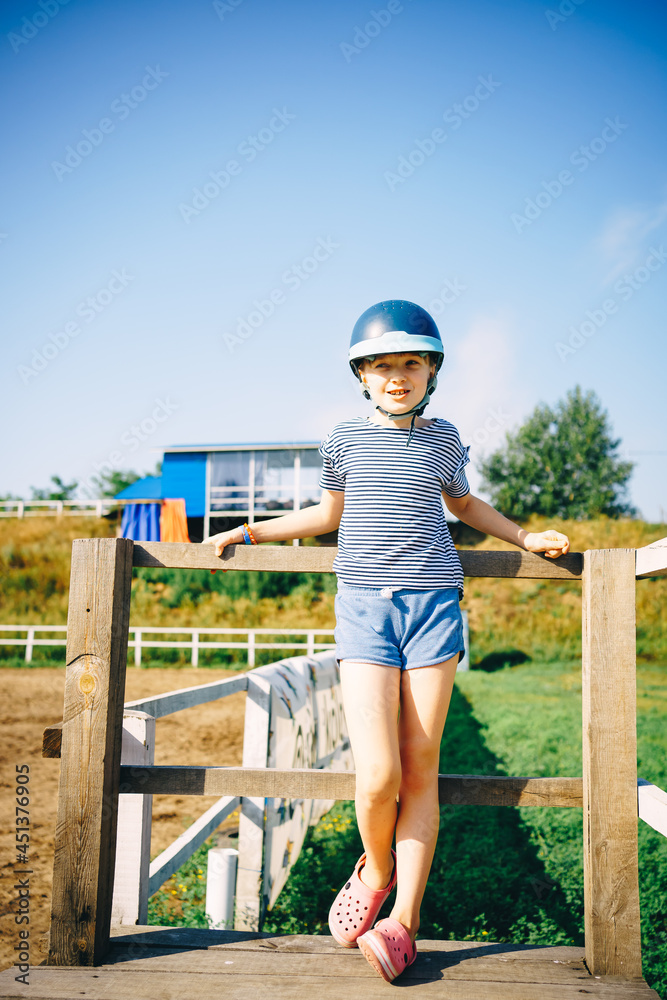 girl jockey in a hat stands by the hedge
