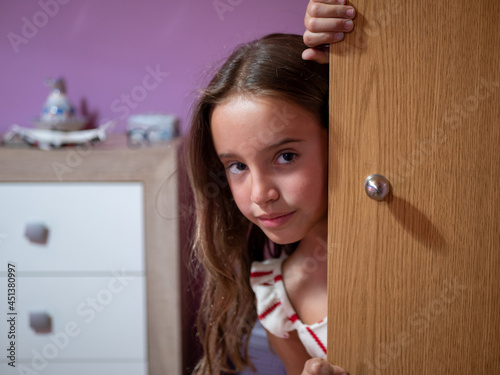 Cute Caucasian girl looking out from behind the wooden door of her bedroom