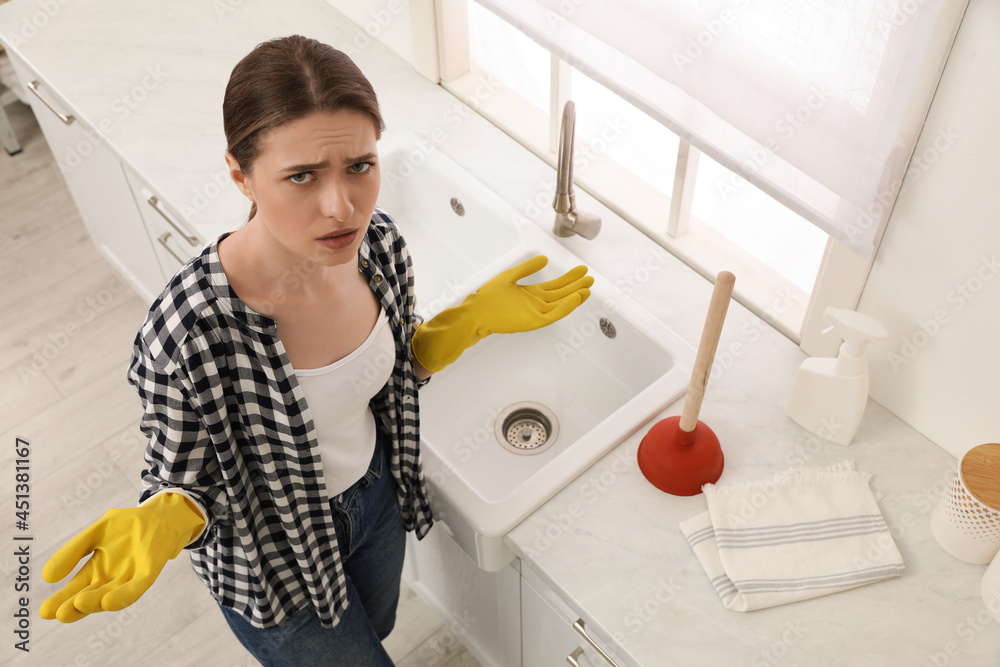 Woman Using Plunger In Kitchen Sink Stock Photo