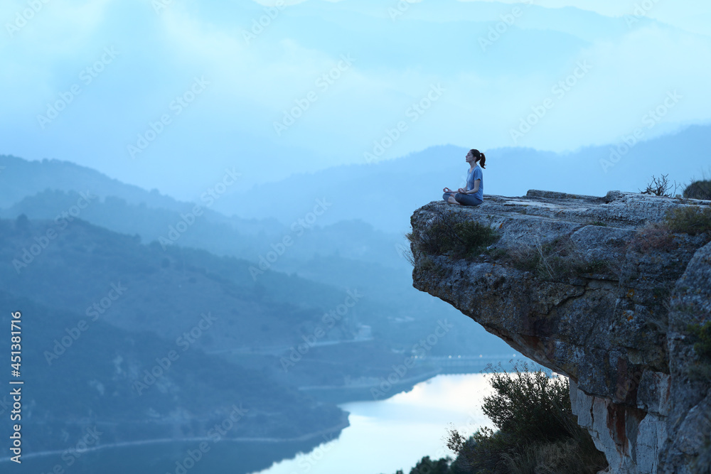 Woman doing yoga exercise in the top of a cliff on blue