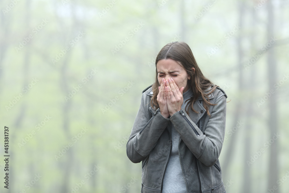 Woman sneezing in a cold foggy park Woman sneezing in a cold foggy park