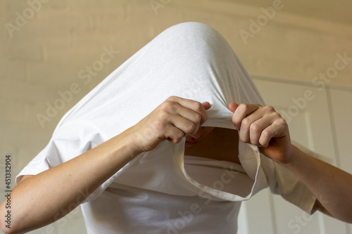 Fotografija The young man pulls his T-shirt over his head,undresses.