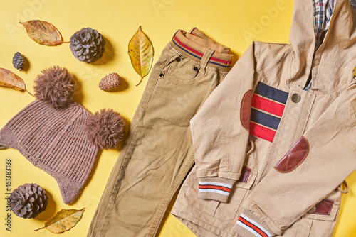 Baby autumn wear clothes on yellow background. Top view. Overhead view of warm kid autumn clothes on colored backdrop
