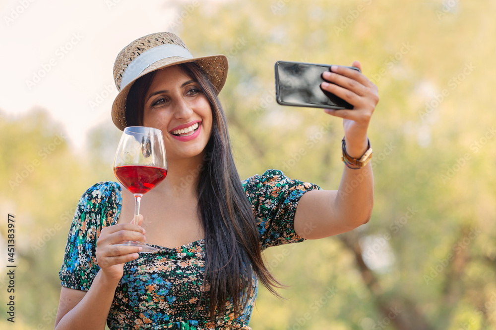 Brunette pretty beautiful caucasian woman in green festive party holiday dress drinking wine from a glass and make selfie with funny faces on her phone. green background Brunette pretty beautiful caucasian woman in green festive party holiday dress drinking wine from a glass and make selfie with funny faces on her phone. green background