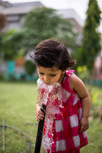 portrait of cute indian baby girl watering in the park.