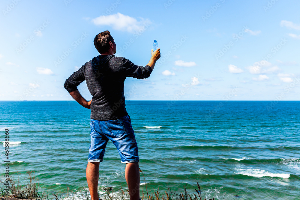 Middle age man relaxing and holding water bottle on the beach after promenade at summer day.Copy space. Middle age man relaxing and holding water bottle on the beach after promenade at summer day.Copy space.