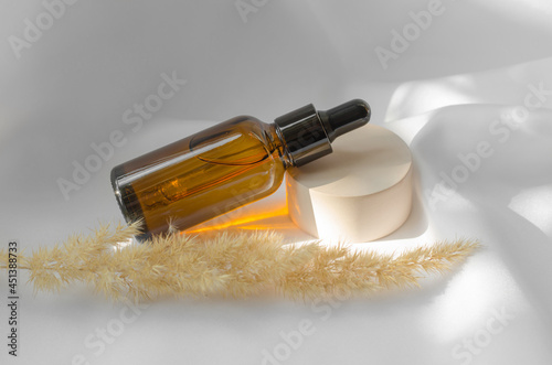 Essential oil or serum in a brown bottle with a dropper. Beauty cosmetics, body care. A bottle of scented oil on the podium and next to a sprig of pampas grass