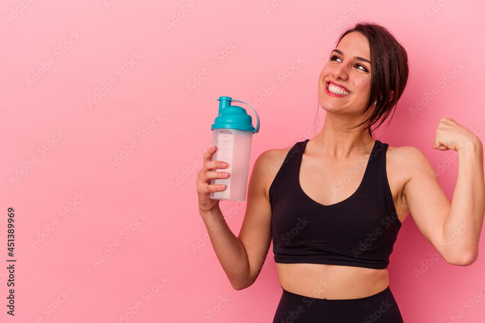 Young caucasian woman drinking a protein shake isolated on pink background raising fist after a victory, winner concept. Young caucasian woman drinking a protein shake isolated on pink background raising fist after a victory, winner concept.