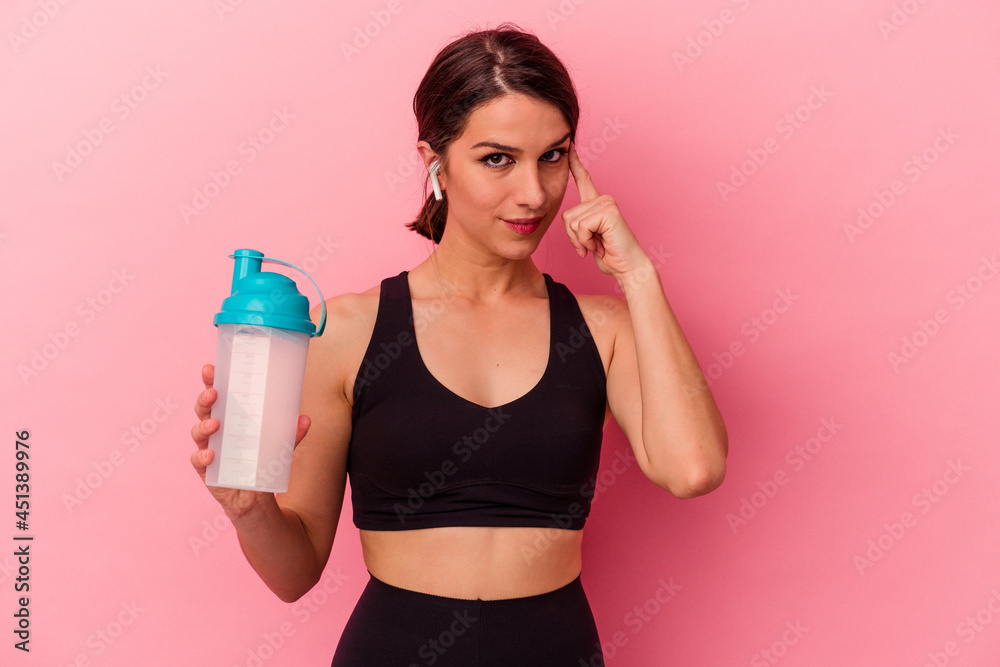 Young caucasian woman drinking a protein shake isolated on pink background pointing temple with finger, thinking, focused on a task.