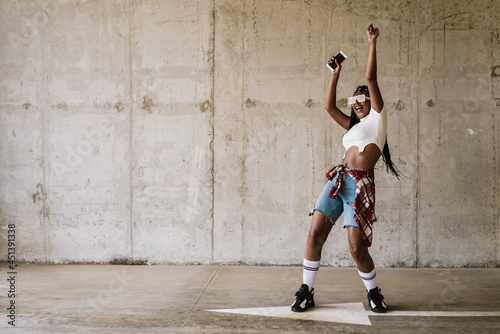 Black young woman dancing and smiling while using mobile phone