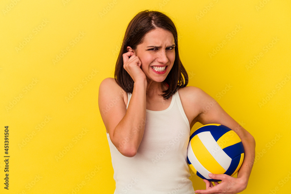 Young caucasian woman playing volleyball isolated on yellow background covering ears with hands.