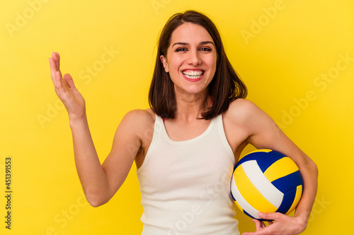 Young caucasian woman playing volleyball isolated on yellow background receiving a pleasant surprise, excited and raising hands.