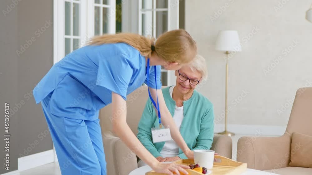Caregiver carries tray puts food on table for old patient