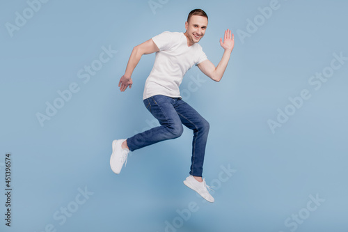 Full body profile side photo of cheerful brown haired attractive man jumping running waving hello isolated over blue color background