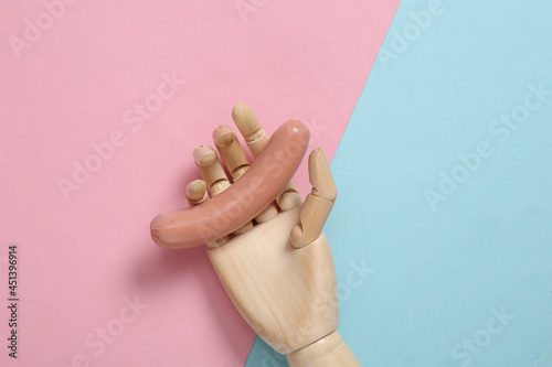 Wallpaper Mural Wooden hand holds a sausage on pink blue background. Minmalistic food concept. Flat lay Torontodigital.ca