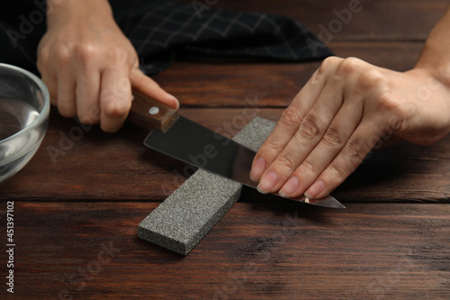 Woman sharpening knife at wooden table, closeup