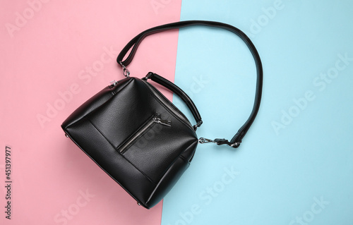 Fashionable leather black handbag on pink blue pastel background. Top view
