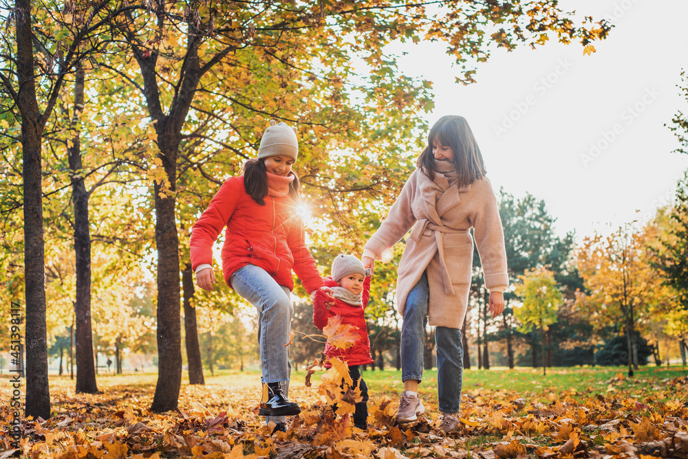 Fototapeta premium Mother and daughter having fun in the autumn park among the falling leaves. Active lifestyle