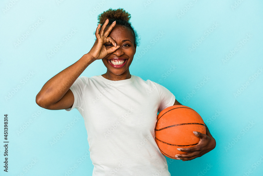 Young african american woman playing basketball isolated on blue background excited keeping ok gesture on eye.