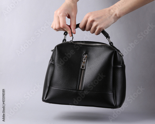 Woman's hand opens black leather bag on gray background