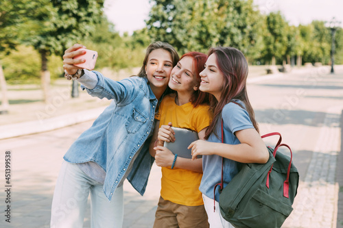 Three charming friends take selfies with their phone on the way to school. The concept of friendship. Education, training, back to school
