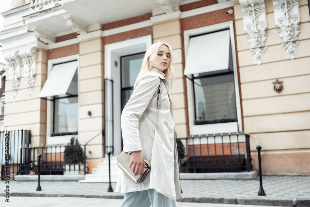 Young fashion blonde woman in a trench coat with a bag in city