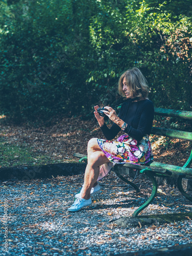 senior active fit caucasian blond woman taking a photograpgh with a compact small mirrorless camera in a park photo