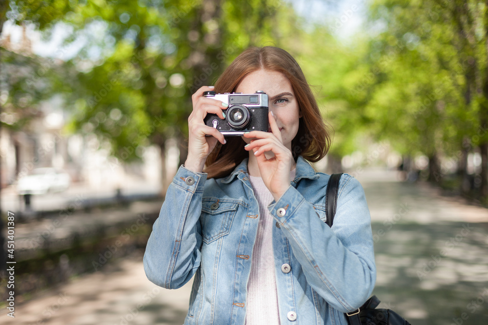 Cute young attractive woman tourist in denim jacket with retro camera in the city