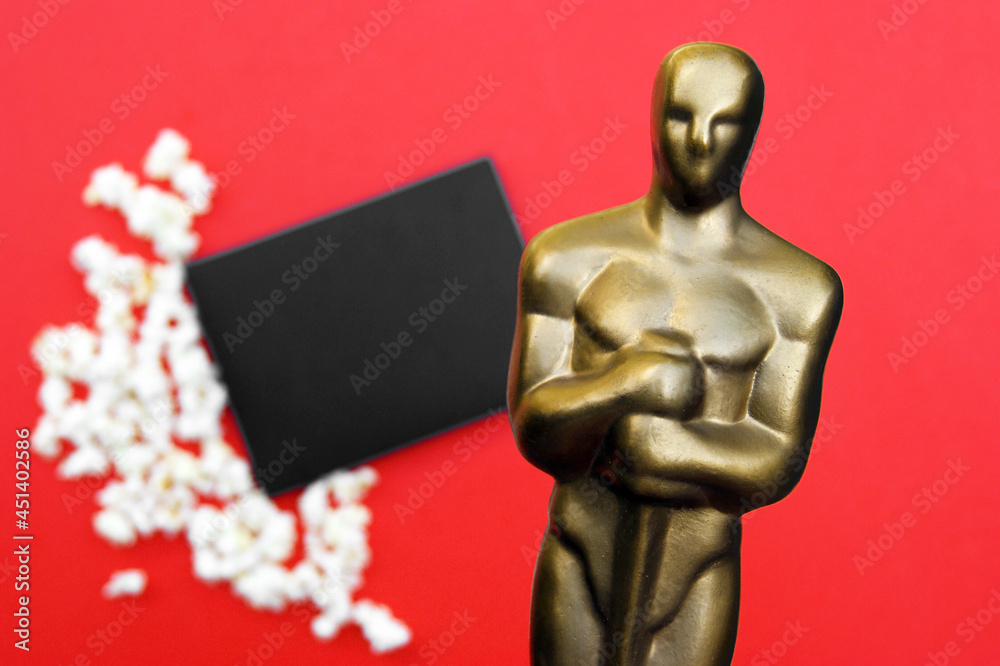 Plastic Oscar award on a red background with popcorn and a black