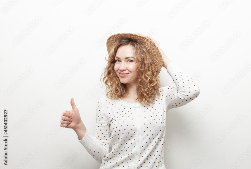 Portrait of cute smiling curly haired Caucasian woman in straw hat showing thumb up on white background Portrait of cute smiling curly haired Caucasian woman in straw hat showing thumb up on white background