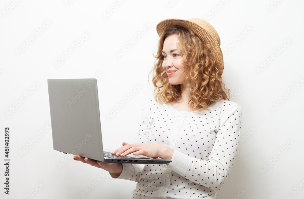 Cute smiling curly-haired caucasian woman in straw hat uses laptop on white background Cute smiling curly-haired caucasian woman in straw hat uses laptop on white background