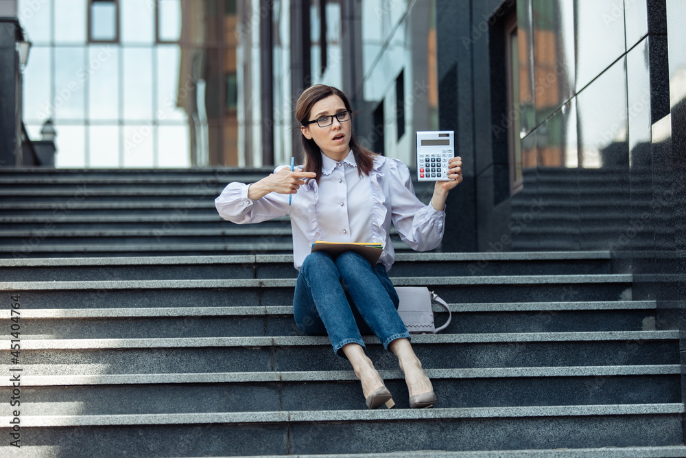 Disheartened business woman is holding a calculator while sitting on the stairs. Lifestyle