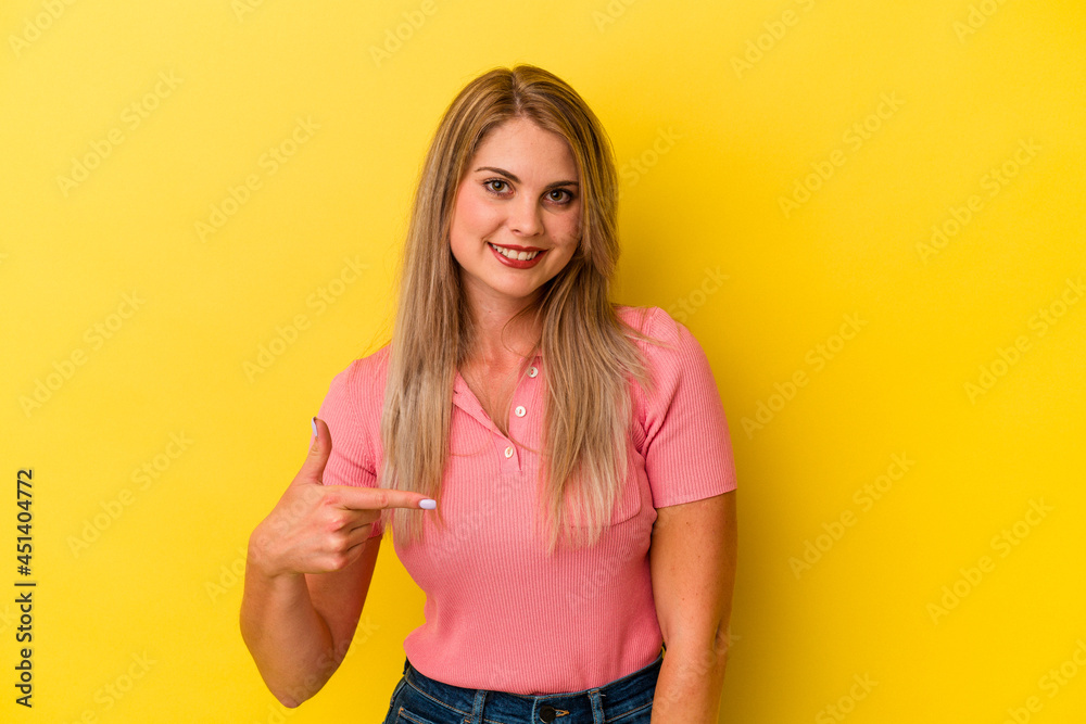 Young russian woman isolated on yellow background person pointing by hand to a shirt copy space, proud and confident