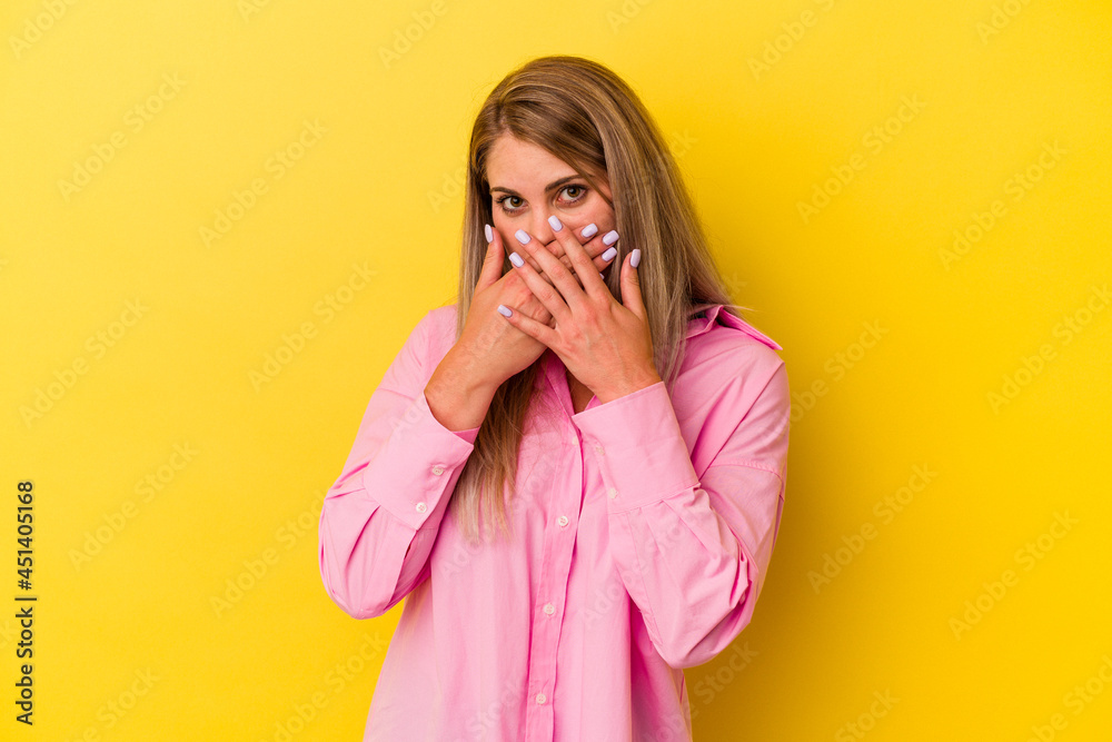 Young russian woman isolated on yellow background covering mouth with hands looking worried. Young russian woman isolated on yellow background covering mouth with hands looking worried.