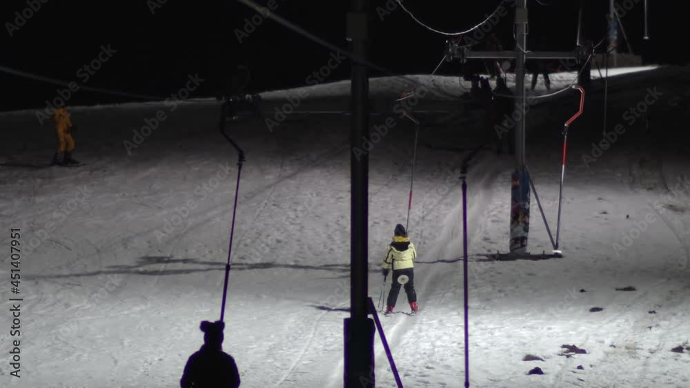 People riding on the button lift, drag lift to the top of the ski slope