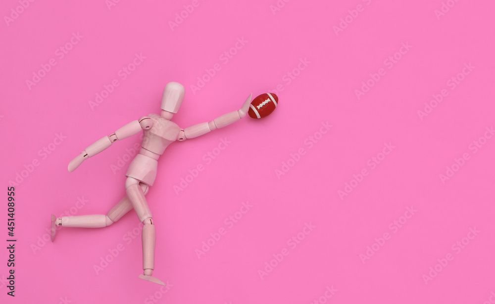 Mini wooden puppet runs with a rugby ball on pink background Mini wooden puppet runs with a rugby ball on pink background