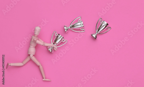 Wooden puppet holding a silver championship cups on pink background