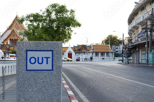 Out word on white frame, blue letter at gray wall besid roade in Bangkok and blur temple background, Thailand. Sign out way frome building. © Kanjana