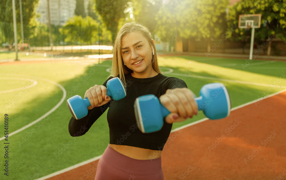 Confident cheerful woman doing punches with dumbbells in stadium Confident cheerful woman doing punches with dumbbells in stadium