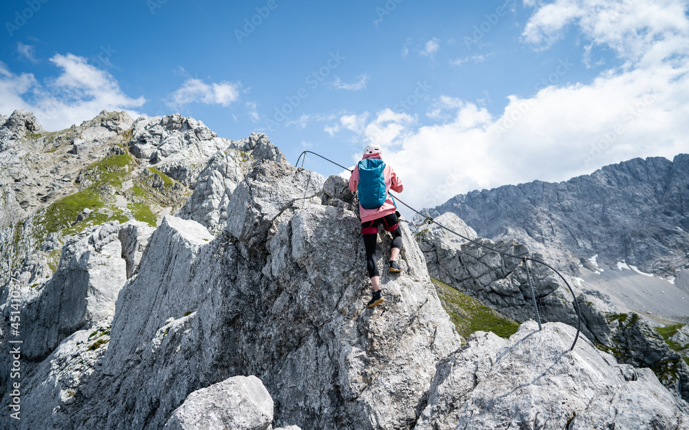 People climbing on steep rock face on via ferrata. Climbers on via ferrata climbing route. Alpine ferrata ascent to a peak or summit. Summer adventure mountain sport activity in alpine landscape.