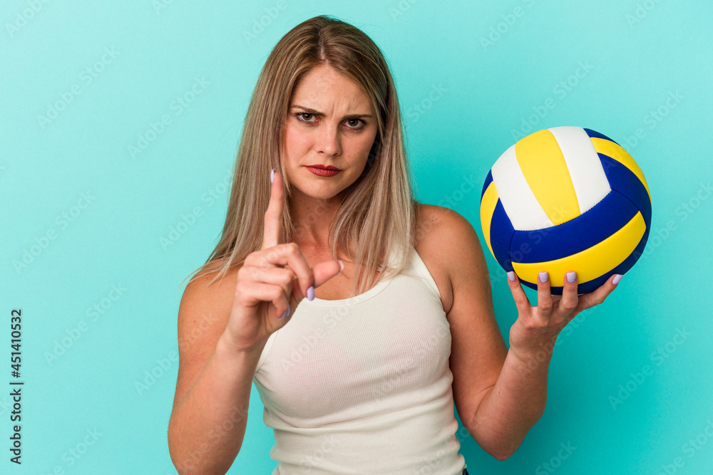 Young russian woman playing volleyball isolated on blue background showing number one with finger.