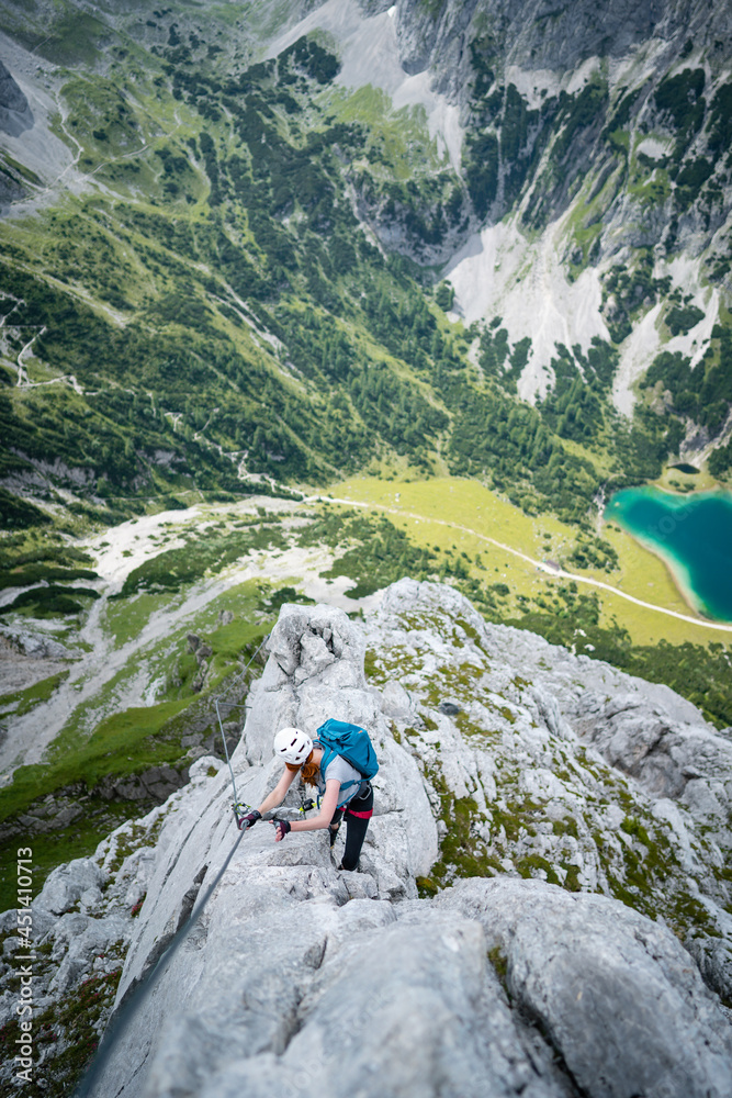 Woman climbs high on rock. Pretty, female climber on a via ferrata - climbing on a rock in Tajatkopf Klettersteig. Taken from mountain Tajakopf near Leermos ehrwald austria alps