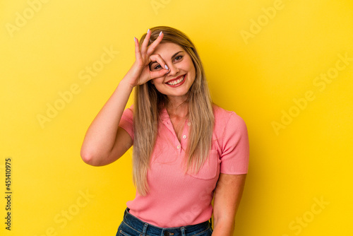 Young russian woman isolated on yellow background excited keeping ok gesture on eye. © Asier